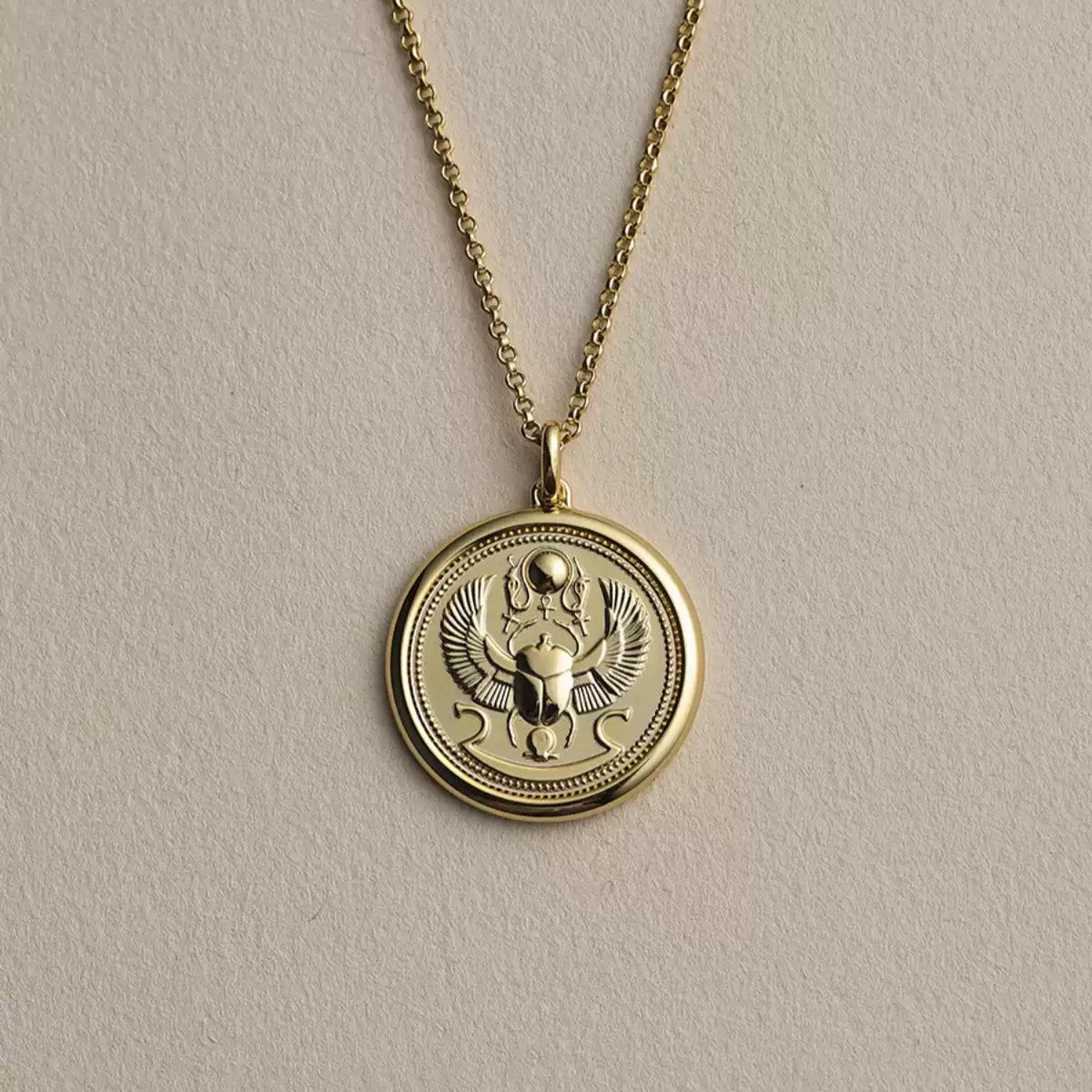 Ancient Egyptian scarab beetle embossed coin pendant necklaces shown in 18K yellow gold and sterling silver finishes with a classic cable chain.