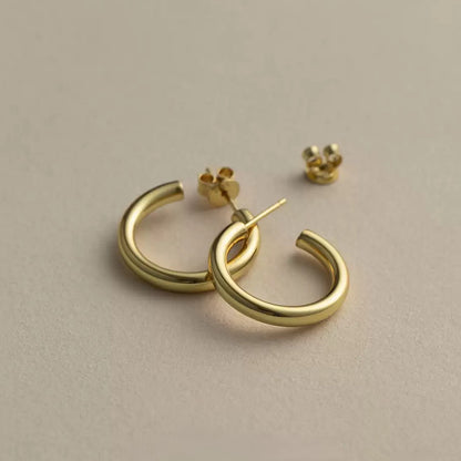 Pair of 18K gold plated 925 sterling silver C-shaped open hoop earrings with a high-polished smooth surface and butterfly backs on a warm neutral background